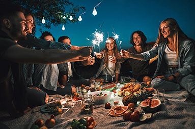 Group of friends, holding sparklers around a picnic table. Group of friends, holding sparklers around a picnic table.