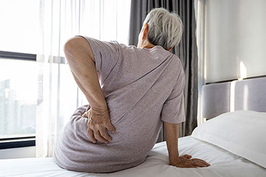 Back side of older person holding lower back in pain.