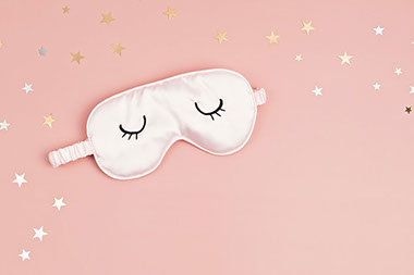 Pink eye mask with closed eyes and gold stars around it.