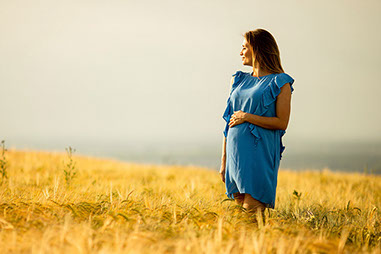 Pregnant women standing in open field.