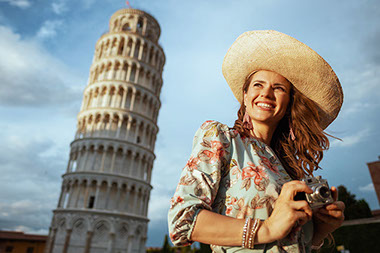 Smiling women standing in front of the Leaning Tower of Pisa, holding a camera.