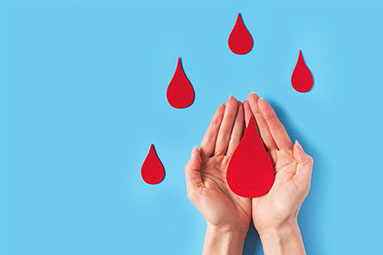 Hands cupped together holding a red paper shaped as a blood drop.