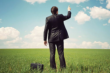 Stress-reducing tips for working healthy. Image of business man in an open field, pointing to the sky.