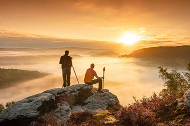 Two men standing on edge of cliff at sunset.