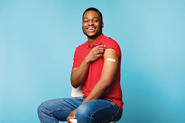 Smiling man showing bandaid on upper arm where he got a vaccine shot.