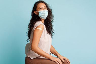 Women wearing face mask covering mouth and nose, with bandaid on upper arm where she received a vaccine shot.
