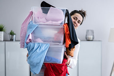 Women carrying 3 large bins over-filled with clothes.