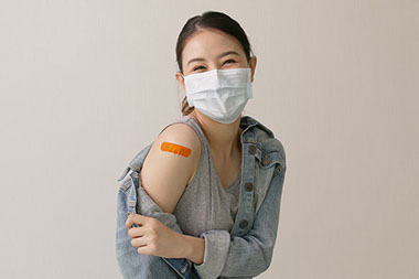 Women wearing face mask, smiling, showing bandage on arm where she got a vaccine.