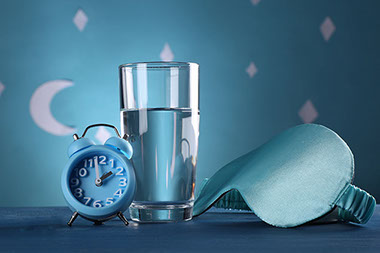 Blue eye mask, alarm clock and glass of water.
