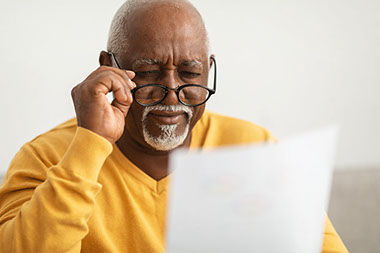 Older man with glasses trying to read a piece of paper.