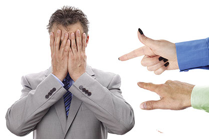 Image of business man covering his face as fingers are pointed at him.