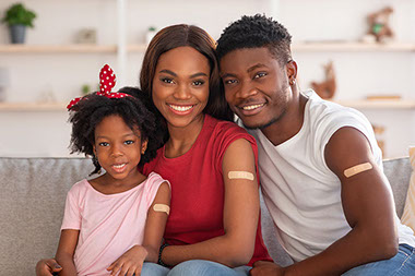 Parents with child all smiling showing upper arm with vaccine bandage.