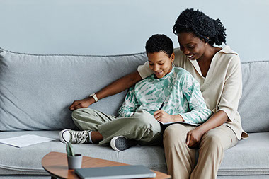 Mother and son sitting while son is writing in a notebook.