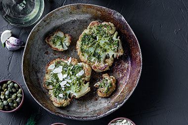 Cauliflower steak with spices, sauce, almond flakes. Capers, olives, herbs, side by side.