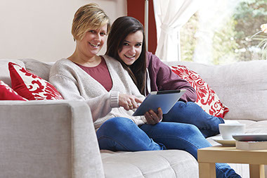Image of mother and daughter sitting on the couch, while mother checks tablet.