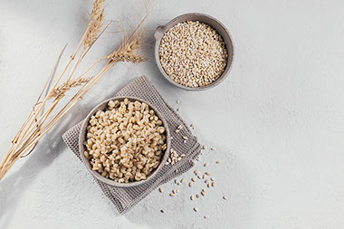 Two bowls filled with barley, one cooked, one raw. Two bowls filled with barley, one cooked, one raw.