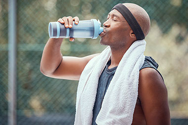 Man with towel behind neck while drinking out of a water bottle. Man with towel behind neck while drinking out of a water bottle.