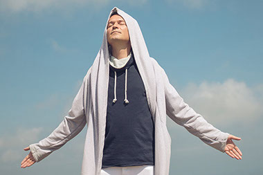 Man standing outside, arms open, eyes closed, breathing fresh air.