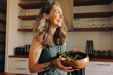 Women smiling while holding a wooden bowl filled with a salad mix. Women smiling while holding a wooden bowl filled with a salad mix.