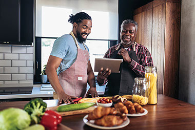 Father and adult son in kitchen cooking together.