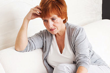 Coping with the loss of a spouse. Image of sad, older female sitting on couch.