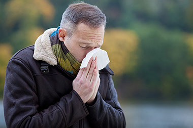 Image of man sneezing into a tissue.