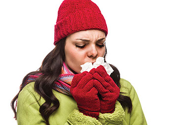 Image of young women dressed warmly coughing into a tissue.