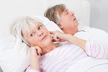 Image of man snoring as spouse is awake plugging her ears.