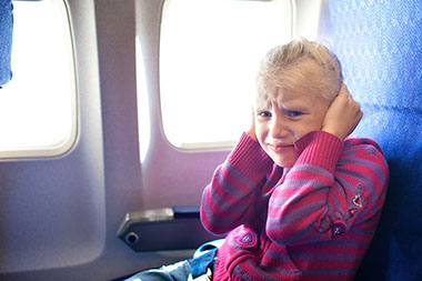 Image of young girl on plane covering her ears.