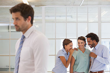 How to steer clear of office gossip. Image of 3 co-workers whispering to each other while another is walking away.