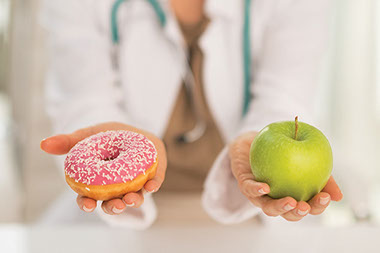 Doctor holding apple in one hand and a donut in the other hand.