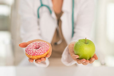 Image of doctor holding a donut in one hand and an apple in the other hand.