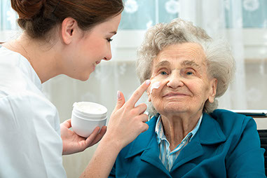 How to care for mature skin Image of a caregiver placing cream on a mature women's face.