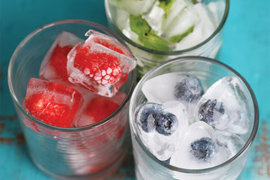 Glasses of water with ice cubes that have berries frozen in them.