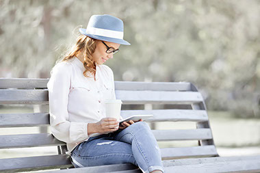 Women on park bench reading and drinking coffee.