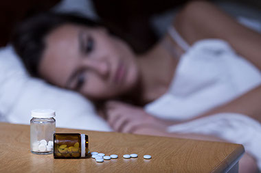 Use Caution with Sleeping Pills. Image of women trying to sleep with pills on her nightstand.
