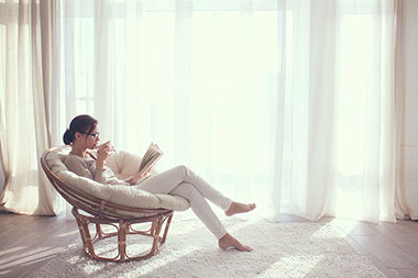 Image of women sitting in a comfortable chair relaxing while reading a book and drinking tea.