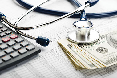 Image of stethoscope and money on top of paper work.