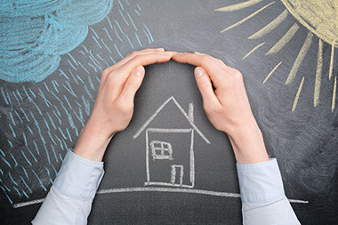 Image of chalkboard drawing of house with hands protecting it from weather elements.