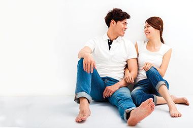 Image of young smiling couple sitting against a wall.