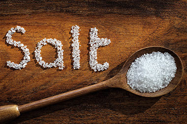 Sea salt on wooden spoon and the word salt written in grain.