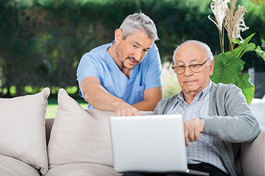 How to choose a quality hospice. Image of male nurse and elderly man on a laptop.