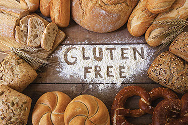 Image of various breads with the words "Gluten Free" written in powedered white flour.
