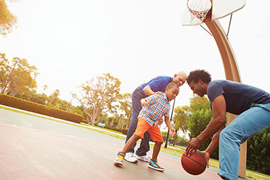 Grandfather, father, and young son playing basketball.
