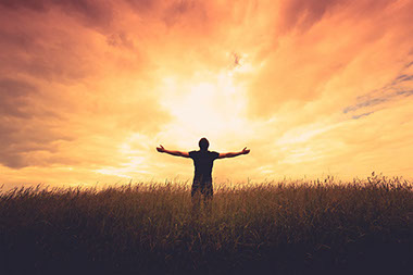 Man holding out arms in the middle of a grass field.