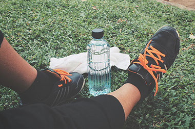 Feet wearing tennis shoes and a bottle of water on grass.