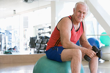 Image of older man sitting on fitness ball holding dumb bells.