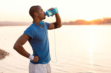 Man standing by a body of water drinking out of a water bottle.