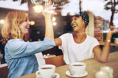 Two friends high-fiving while sitting at a cafe.