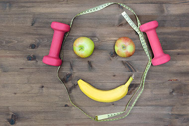 Apples, measuring tape, dumbbells and banana assembled into a smiling face. Apples, measuring tape, dumbbells and banana assembled into a smiling face.